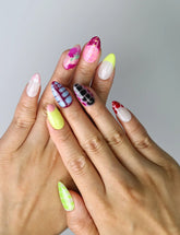 Hand model wearing medium almond press-on nails in vibrant pink, purple, yellow, and red for a bold, artistic look